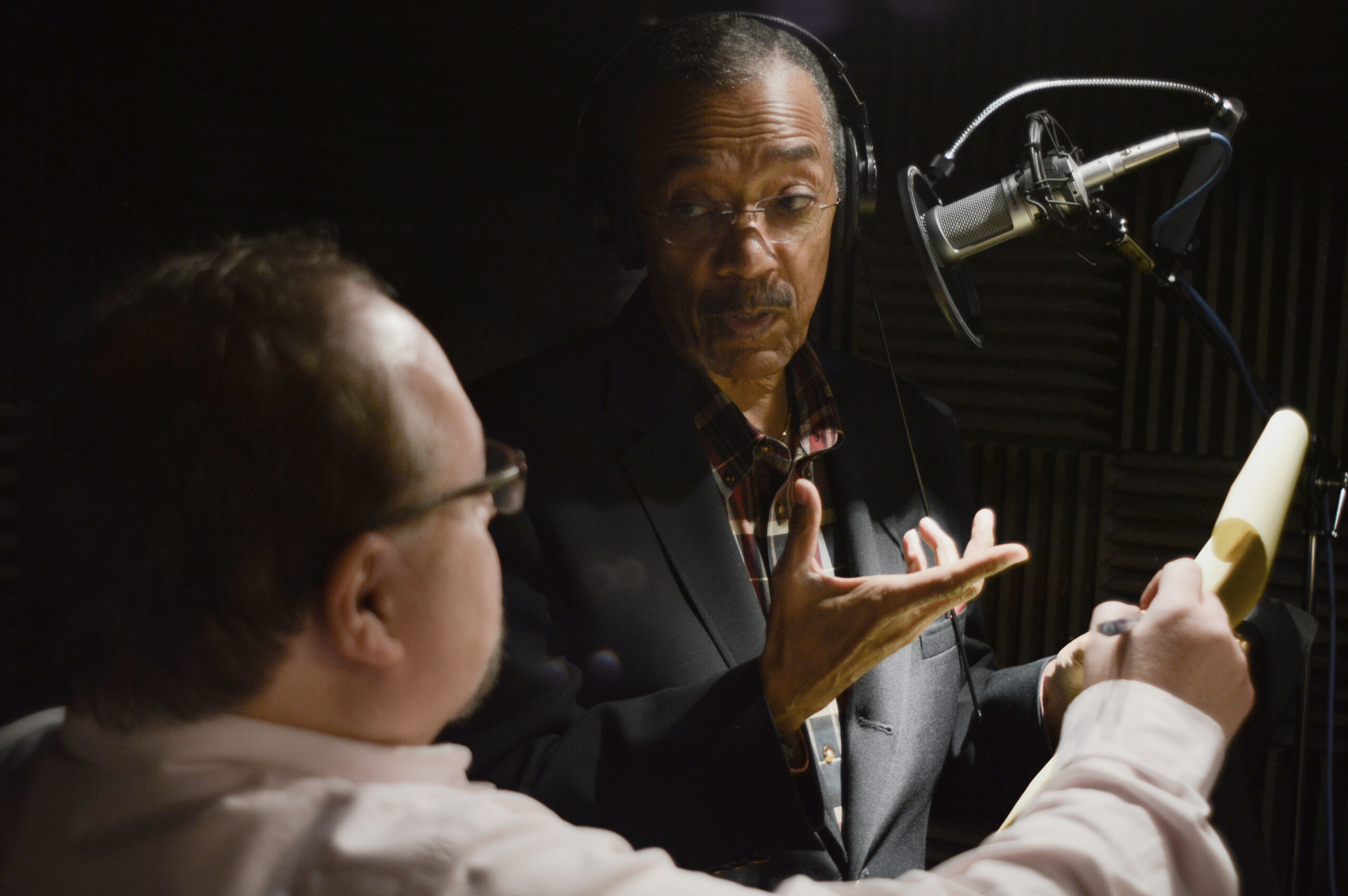 A man in headphones talking to another man.