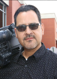 A man with sunglasses holding a camera.