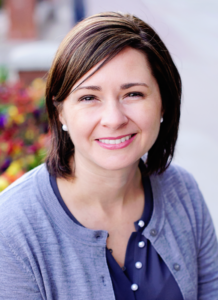 A woman with brown hair and blue shirt smiling.